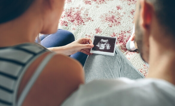 Couple looking at ultrasound of their baby sitting on the bed. Selective background focus on ultrasound.
